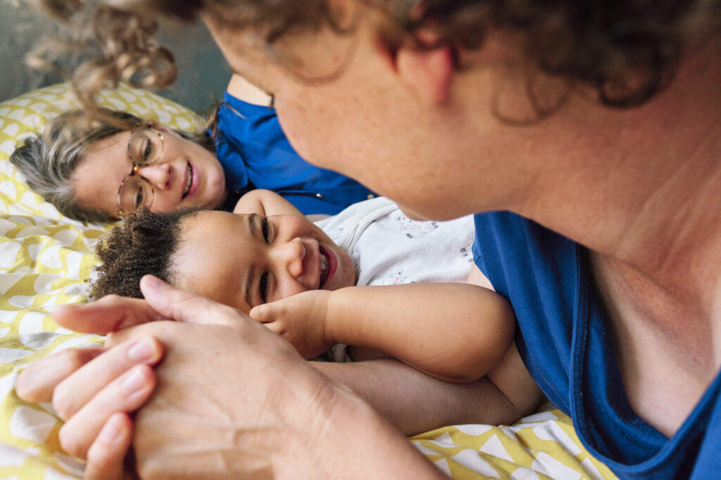 Two moms lying on the bed with their son in London is an example of my inclusive and LGBTQI+ friendly family photography business. 