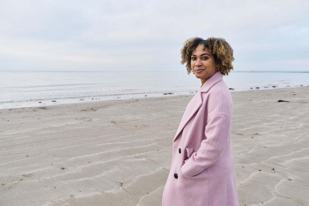 what to wear to your photo session also depends on the location, like this woman is wearing a pink coat on a winter beach. 