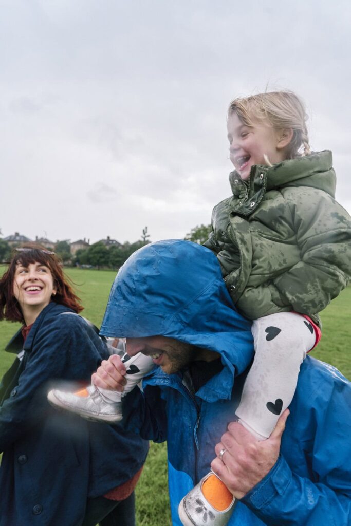 A family walking through Peckham Park together in rain coats. 
