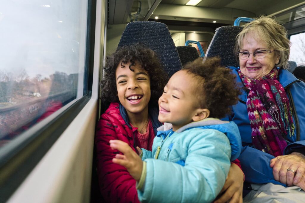Natural family moment with siblings and grandmother laughing on a train during photo session