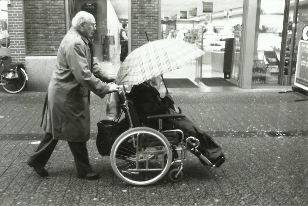 Grandfather joyfully pushing a wheelchair down the high street, showing his playful spirit in this generational family photo.